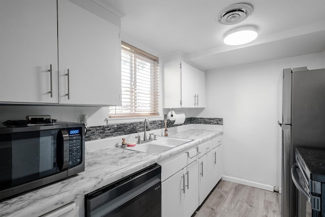 kitchen featuring appliances with stainless steel finishes, a sink, light wood-style floors, white cabinets, and light countertops
