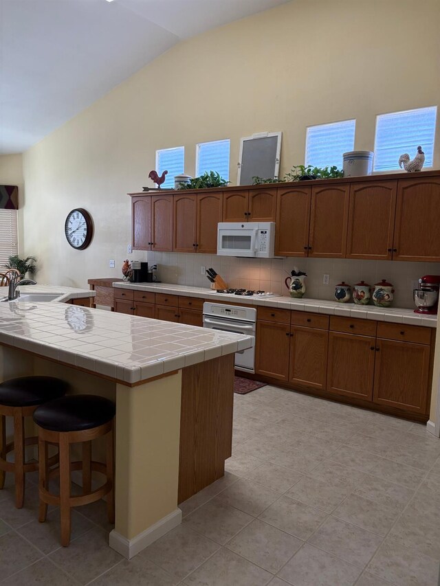 2644 Gibson Ave, Clovis, CA 93611 - kitchen featuring white appliances, a sink, tile countertops, high vaulted ceiling, and decorative backsplash