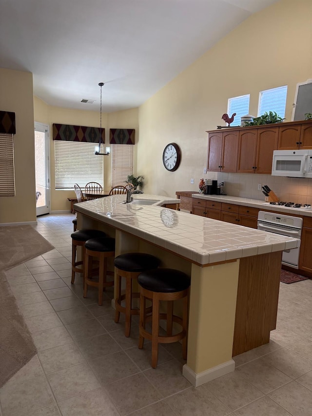 2644 Gibson Ave, Clovis, CA 93611 - kitchen featuring white appliances, light tile patterned floors, tile counters, a kitchen bar, and decorative backsplash