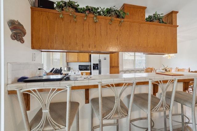 5532 N Cleo Ave, Fresno, CA 93722 - kitchen featuring white fridge with ice dispenser, a peninsula, tile counters, and brown cabinetry