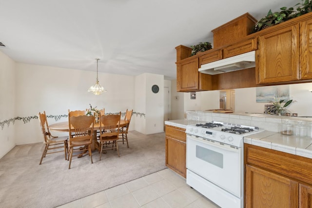 5532 N Cleo Ave, Fresno, CA 93722 - kitchen featuring white range with gas cooktop, under cabinet range hood, light colored carpet, tile countertops, and brown cabinetry