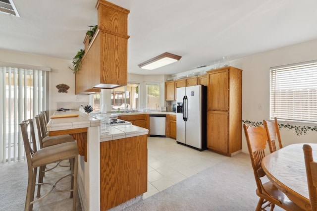 5532 N Cleo Ave, Fresno, CA 93722 - kitchen featuring fridge with ice dispenser, dishwasher, a peninsula, tile countertops, and light carpet