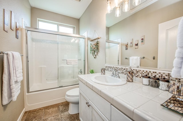 bathroom featuring vanity, toilet, decorative backsplash, enclosed tub / shower combo, and baseboards