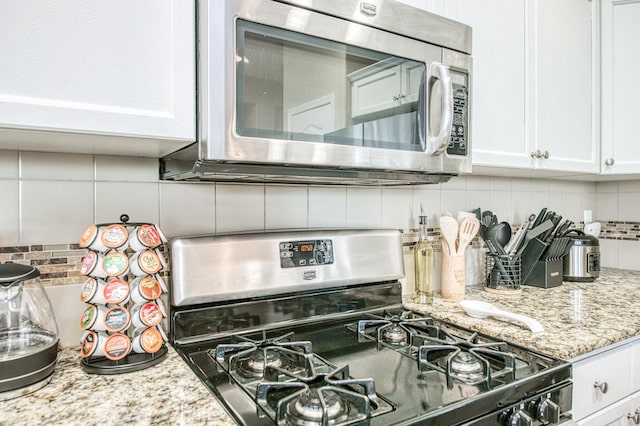 kitchen view of stainless steel appliances, backsplash, light stone countertops, and white cabinetry