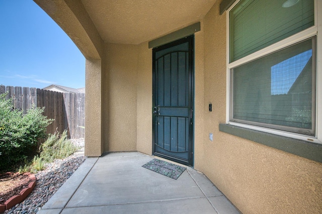 entrance to property featuring stucco siding, fence, and a patio area
