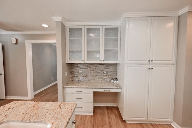 kitchen with light wood finished floors, baseboards, glass insert cabinets, decorative backsplash, and crown molding