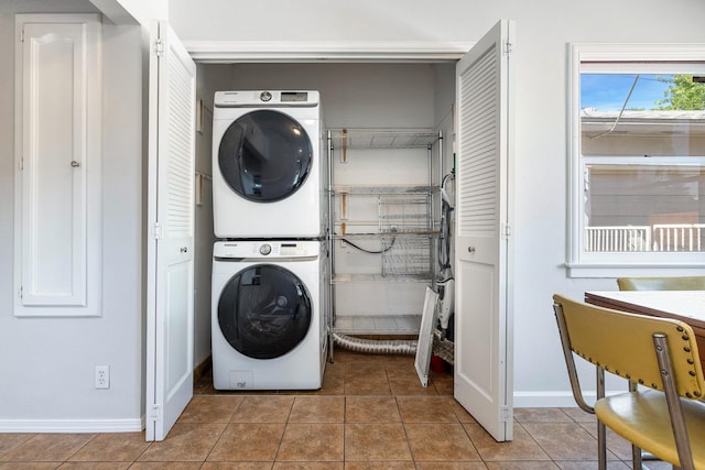 clothes washing area featuring stacked washer and clothes dryer, baseboards, and light tile patterned floors