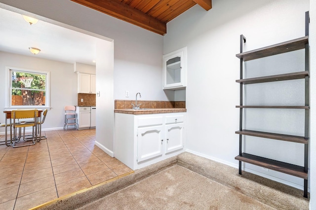 kitchen with wooden ceiling, white cabinets, beamed ceiling, a sink, and baseboards