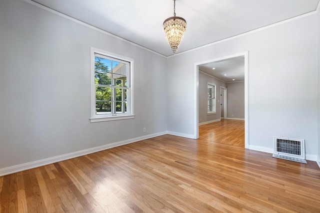 empty room with ornamental molding, a chandelier, light wood-style floors, and baseboards