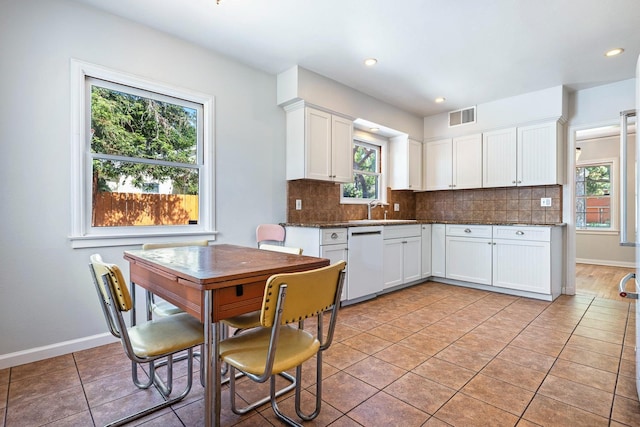 kitchen with white dishwasher, a sink, decorative backsplash, white cabinetry, and baseboards