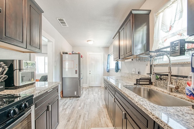 4487 E Bend Ave, Fresno, CA 93702 - kitchen featuring a sink, freestanding refrigerator, light wood-style floors, dark brown cabinets, and a textured ceiling