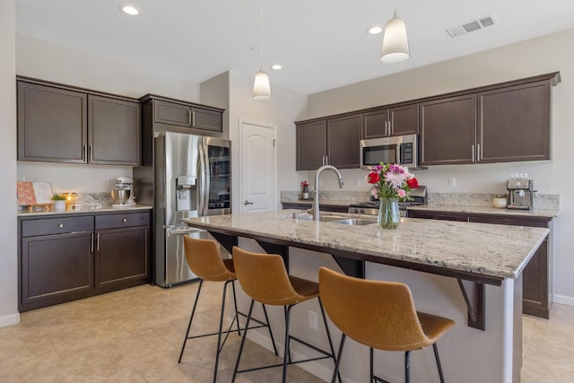 6326 W Sweet Ct, Visalia, CA 93291 - kitchen featuring stainless steel appliances, dark brown cabinets, light stone counters, hanging light fixtures, and a kitchen bar