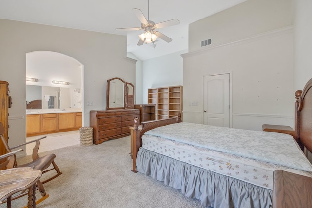 bedroom featuring light carpet, high vaulted ceiling, ensuite bathroom, and a ceiling fan