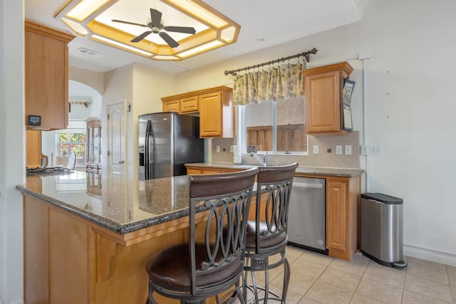 kitchen featuring appliances with stainless steel finishes, tasteful backsplash, a ceiling fan, a breakfast bar, and light tile patterned floors
