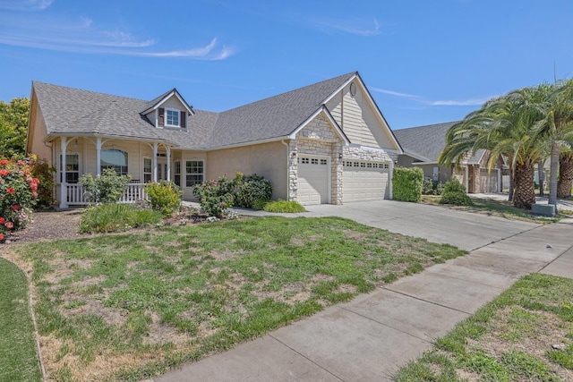 view of front of house with a porch, an attached garage, driveway, stone siding, and a front lawn