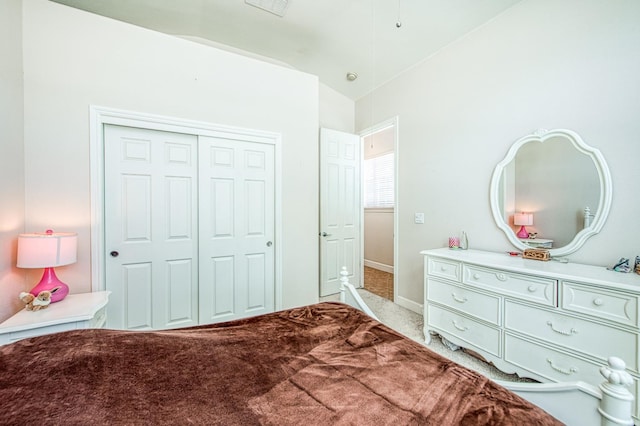 bedroom with vaulted ceiling, light carpet, a closet, and baseboards