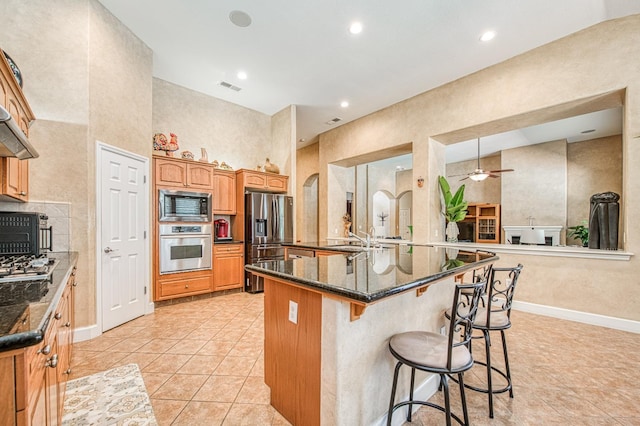 kitchen with stainless steel appliances, a kitchen bar, a sink, a ceiling fan, and dark stone counters