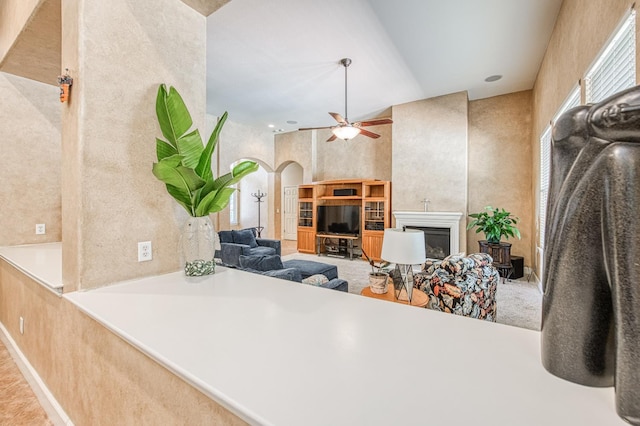 living room with a glass covered fireplace, a ceiling fan, and arched walkways