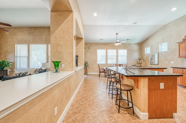 kitchen featuring ceiling fan, a kitchen bar, light tile patterned floors, a sink, and a kitchen island with sink