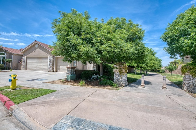view of property hidden behind natural elements featuring a garage, concrete driveway, stucco siding, and stone siding