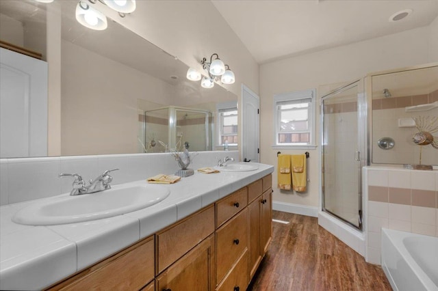 bathroom featuring a shower stall, wood finished floors, a bath, and double vanity