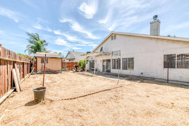 2670 N Katy Ave, Fresno, CA 93722 - rear view of house featuring a fenced backyard, an outdoor structure, a shed, stucco siding, and a chimney