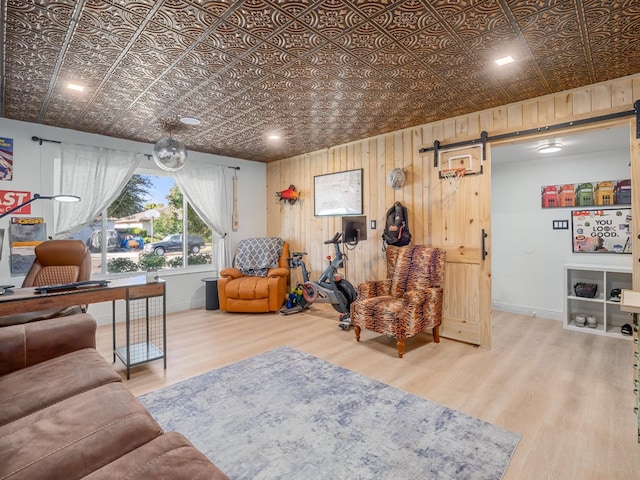 living area with a barn door, an ornate ceiling, wood finished floors, wooden walls, and baseboards