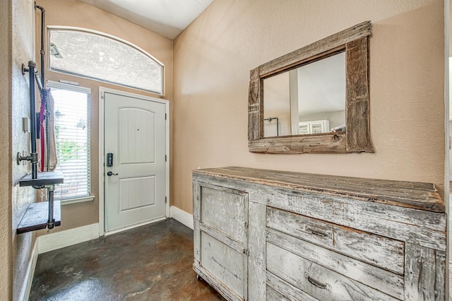 foyer featuring finished concrete flooring, baseboards, and a textured wall