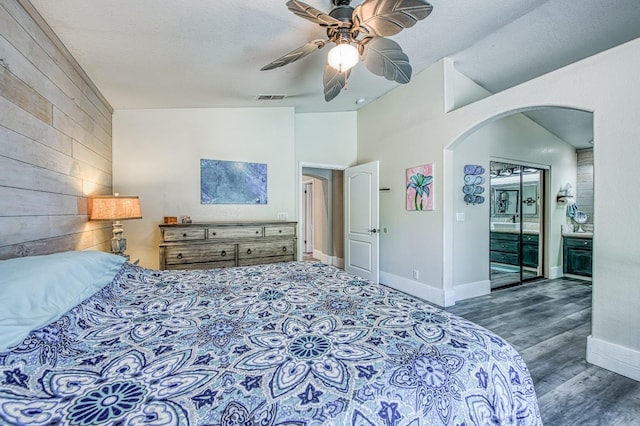 bedroom with arched walkways, vaulted ceiling, wood finished floors, baseboards, and wooden walls