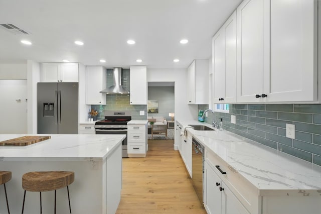 kitchen with appliances with stainless steel finishes, wall chimney exhaust hood, a sink, light wood-type flooring, and backsplash