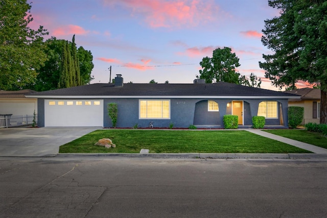 ranch-style house featuring driveway, stucco siding, a garage, a lawn, and a chimney
