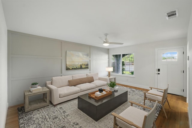 living area featuring ceiling fan, wood finished floors, a decorative wall, and baseboards