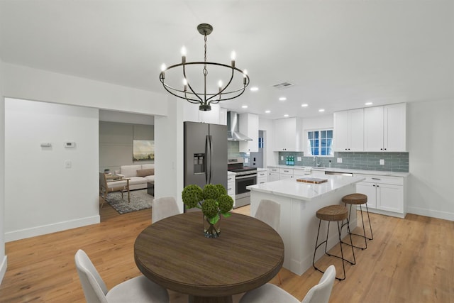 kitchen with stainless steel appliances, a sink, wall chimney range hood, decorative backsplash, and a chandelier