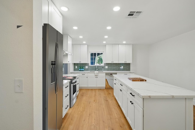 kitchen with appliances with stainless steel finishes, a center island, tasteful backsplash, a sink, and white cabinetry