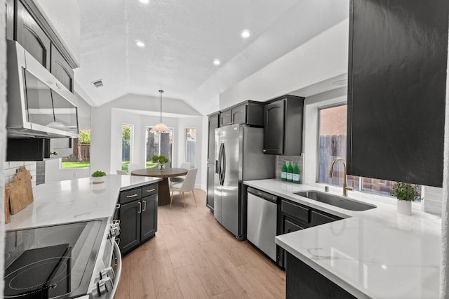 kitchen featuring appliances with stainless steel finishes, a sink, lofted ceiling, tasteful backsplash, and light wood-style flooring