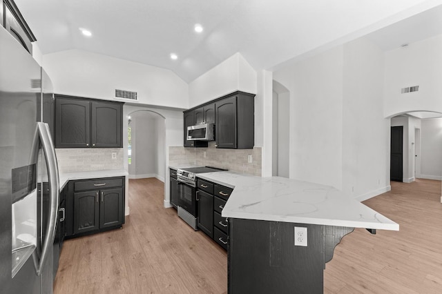kitchen with arched walkways, appliances with stainless steel finishes, a peninsula, recessed lighting, and high vaulted ceiling
