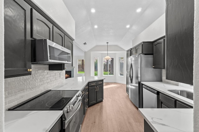 kitchen with appliances with stainless steel finishes, vaulted ceiling, light wood finished floors, backsplash, and light stone counters