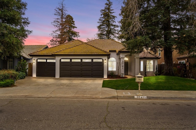 mediterranean / spanish-style house featuring an attached garage, driveway, stucco siding, a yard, and a tiled roof