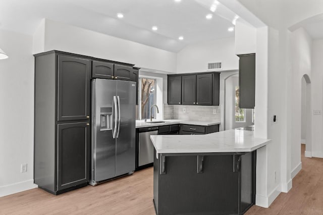kitchen with stainless steel appliances, a sink, a peninsula, arched walkways, and decorative backsplash