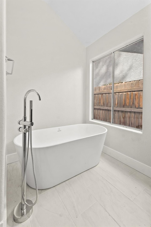bathroom with vaulted ceiling, a soaking tub, and marble finish flooring