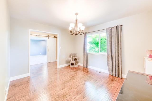 spare room with a chandelier, light wood-type flooring, a barn door, and baseboards