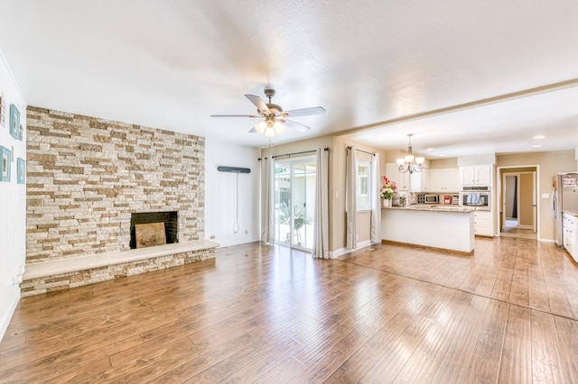 unfurnished living room with a chandelier, ceiling fan, a stone fireplace, and light wood finished floors