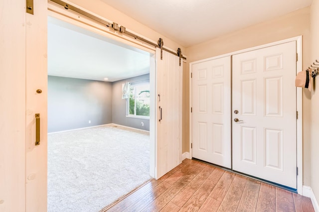 entryway with a barn door, light wood finished floors, baseboards, and light colored carpet