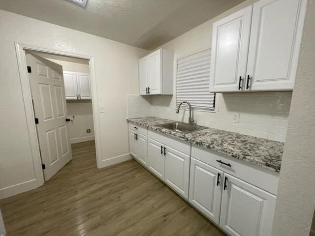 kitchen with a sink, baseboards, white cabinetry, and light wood-style floors