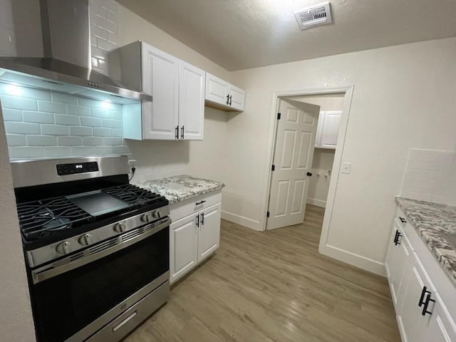 kitchen with gas range, wall chimney exhaust hood, light wood finished floors, decorative backsplash, and white cabinets