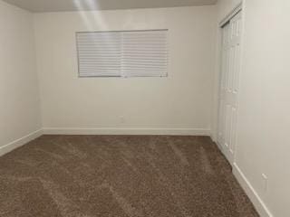 unfurnished bedroom featuring dark carpet, baseboards, and a closet