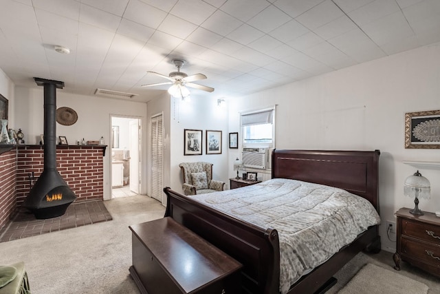 bedroom with carpet, a wood stove, a closet, ceiling fan, and connected bathroom
