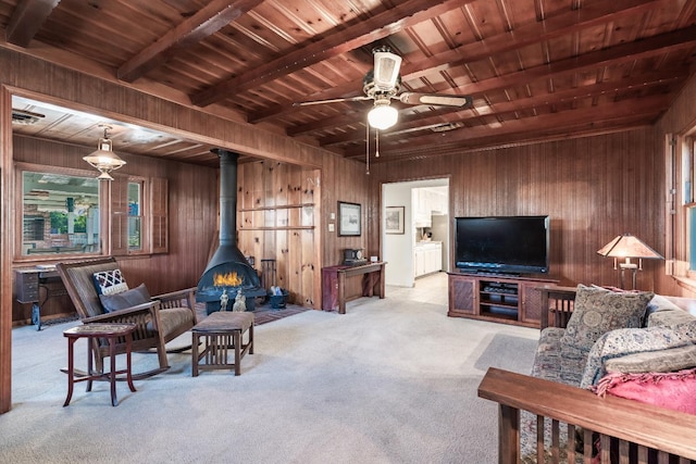 living room with wood walls, carpet, wood ceiling, a wood stove, and a ceiling fan
