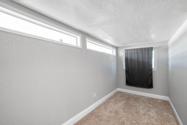 carpeted spare room with a textured ceiling and baseboards
