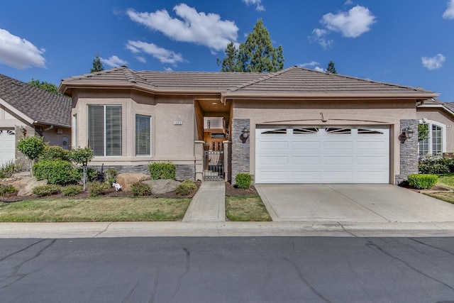view of front of property featuring stone siding, a tiled roof, a garage, driveway, and a gate